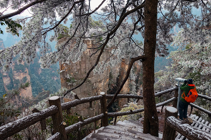 Shorty using a scope to look out over the mountains when visiting Zhangjiajie in China. You can see the floating pillars covered in snow from there down an ornate stairway