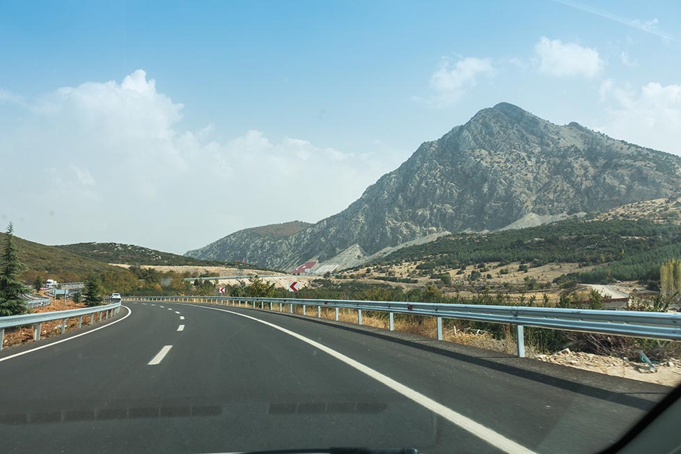 A road with a large mountain in the distance and a blue sunny sky in Albania Guide to public transport in Albania and renting a car and hitchhiking