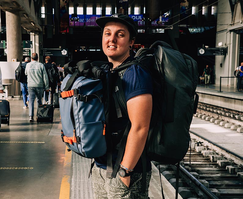 Nic standing in a train station with a front and backpack on Thailand backpacking packing list guide.