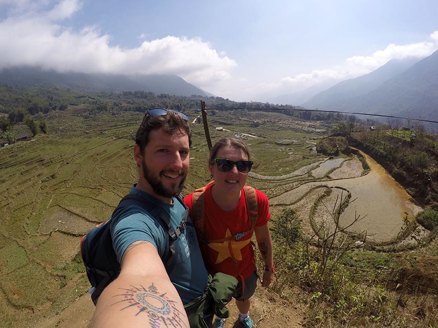Nic and Shorty taking a selfie with a rice paddy behind them and mountains in the distance in Vietnam