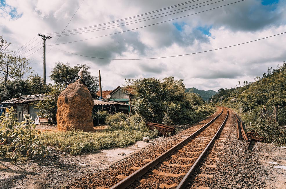 Train tracks running through a remote rural village and small house in Vietnam with mountains in the distance