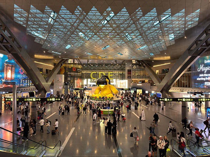 The large main area of Hamad International Airport with the massive yellow bear and lamp sculpture in the middle of the terminal in Doha, Qatar