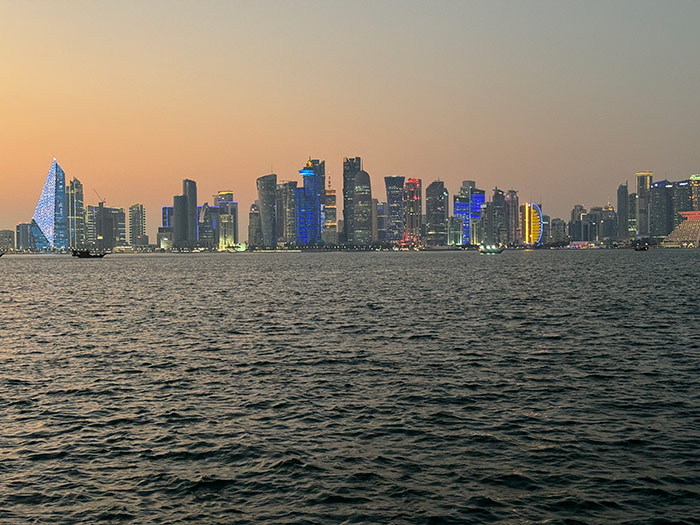 The skyline of West Bay lit up with an orange sunset behind it from across the harbour in Doha, Qatar