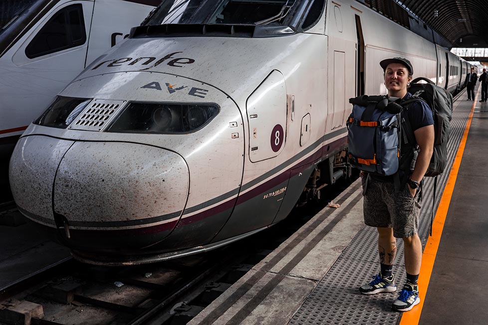 Nic standing on a train platform with their backpacks in Europe.