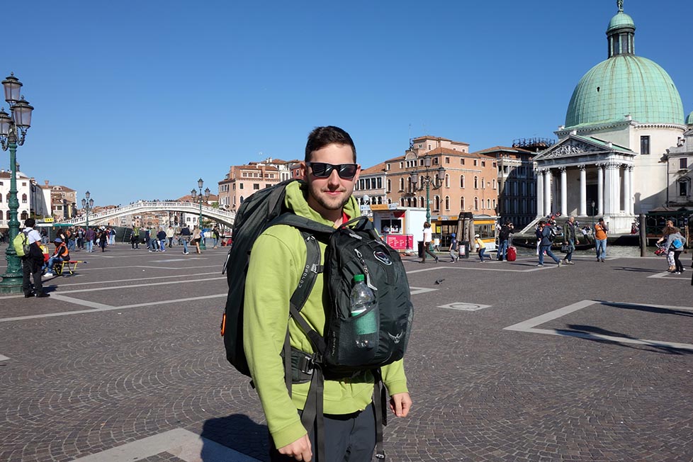Shorty standing with his backpacks in a square in Venice in Italy