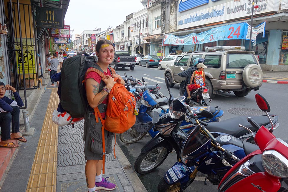 Nic standing on the street with two backpacks on next to some scooters in Thailand
