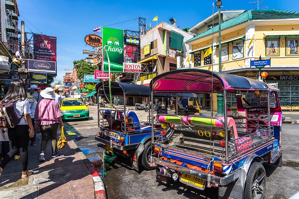 Two brightly coloured tuk tuks wait at the end of Khao San Road in Bangkok, Thailand