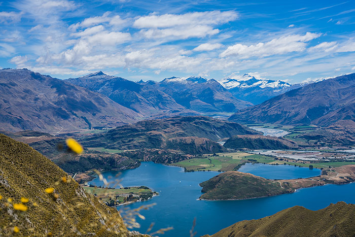 The view from Roys Peak near wanaka and Queenstown in New Zealand with blue lakes at the bottom and snow covered peaks in the distance