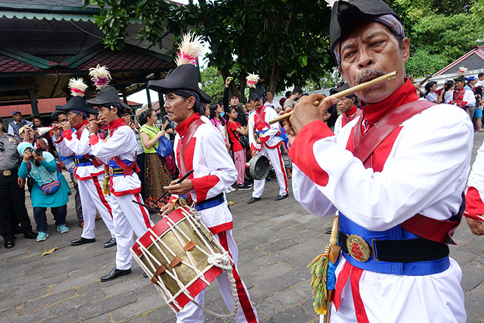 Men in a parade at the Royal palaces in Yogyakarta, Indonesia. They are wearing traditional clothing and playing instruments as they march
