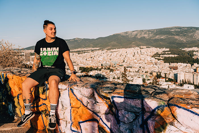 Nic sitting on a wall on a view point over Athens, Greece with the city and mountains in the distance