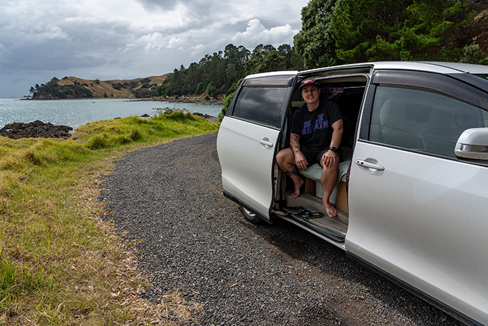 Nic sitting inside a campervan on a coastal road in New Zealand