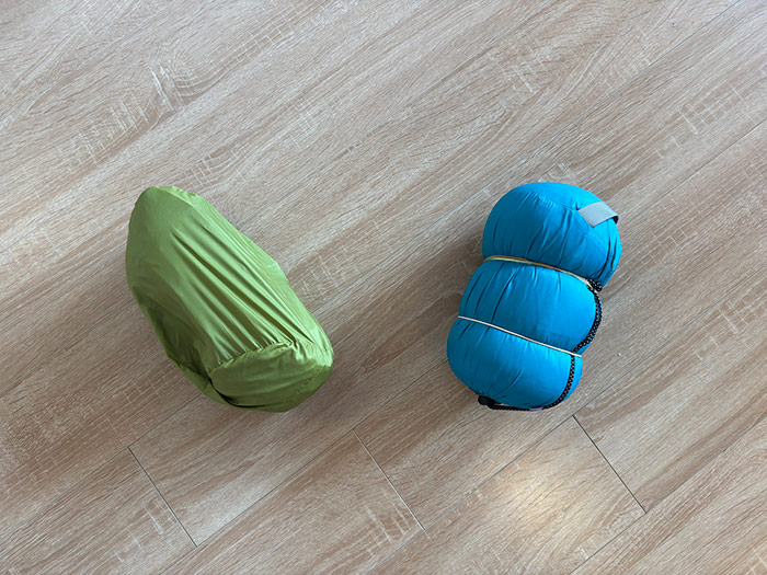 A waterproof jacket and a hoodie laid out on the floor below, and across are the waterproof jacket and hoodie packed down into their packing sacks.
