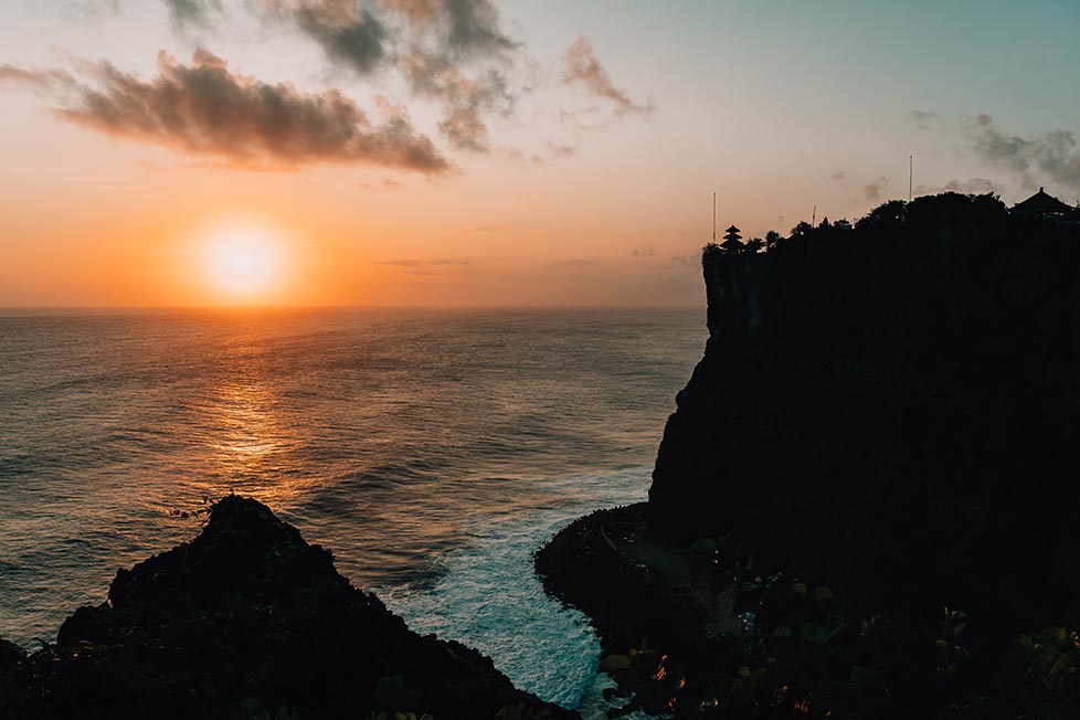 Sunset over the ocean at Uluwatu temple in Bali with the temple visible on the cliffs