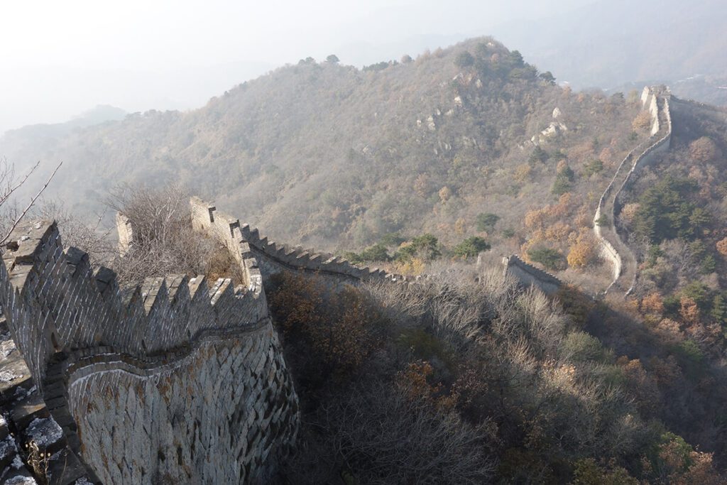 A wild and unkept section of the Great Wall of China near Mutianyu. you can see overgrow trees and bushes in the wall and mountains in the distance